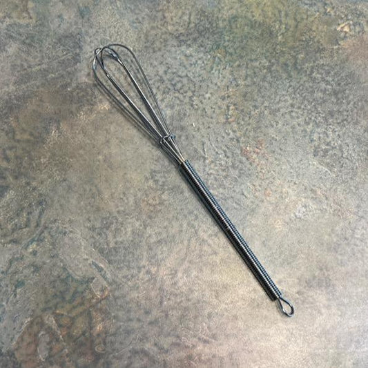 A small stainless steel whisk lying on a textured surface.