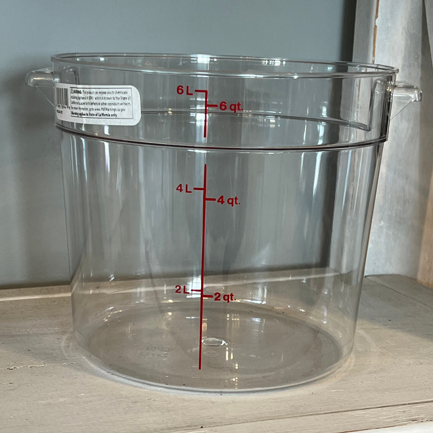 A clear plastic mixing bowl with measurement markings, featuring two handles