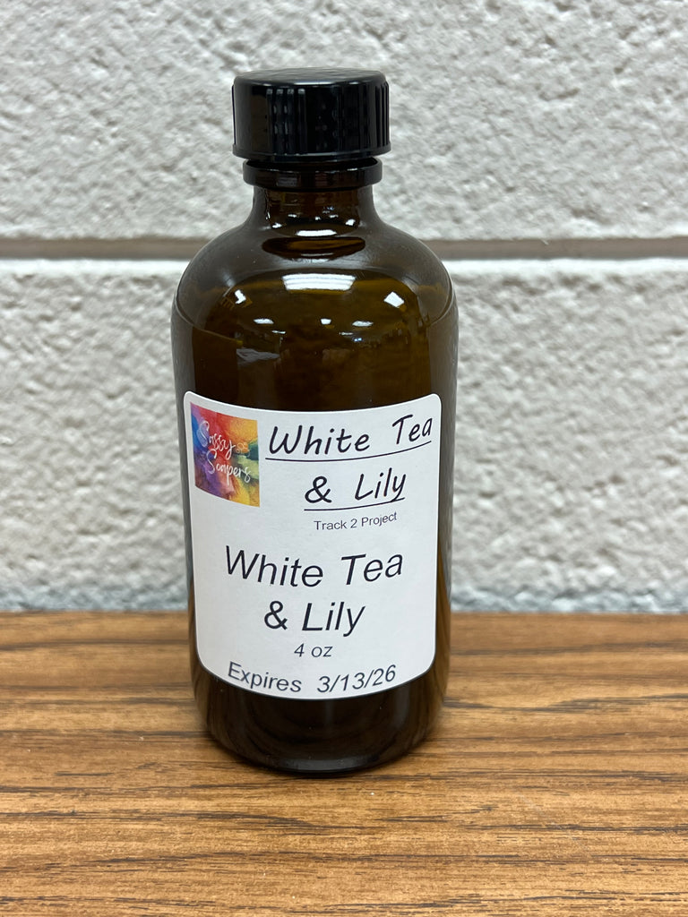4 oz Bottle of White Tea & Lily fragrance oilon a wooden surface with a white wall background.  Expires 3/12/2026