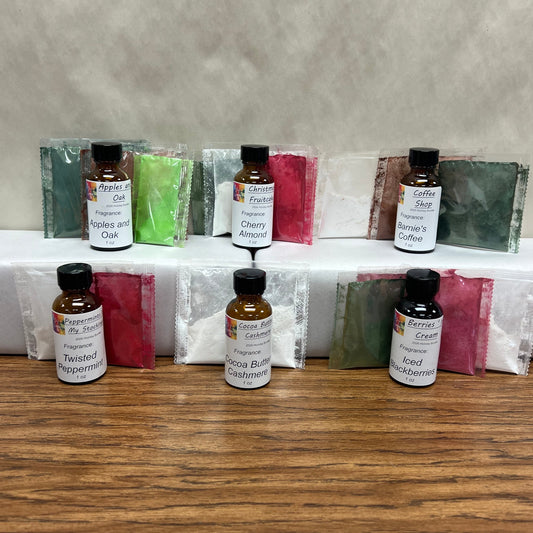 A set of small amber glass bottles with black caps and white labels, arranged on a white shelf with colorful powder packets behind them, all placed on a wooden tabletop against a textured beige wall.
