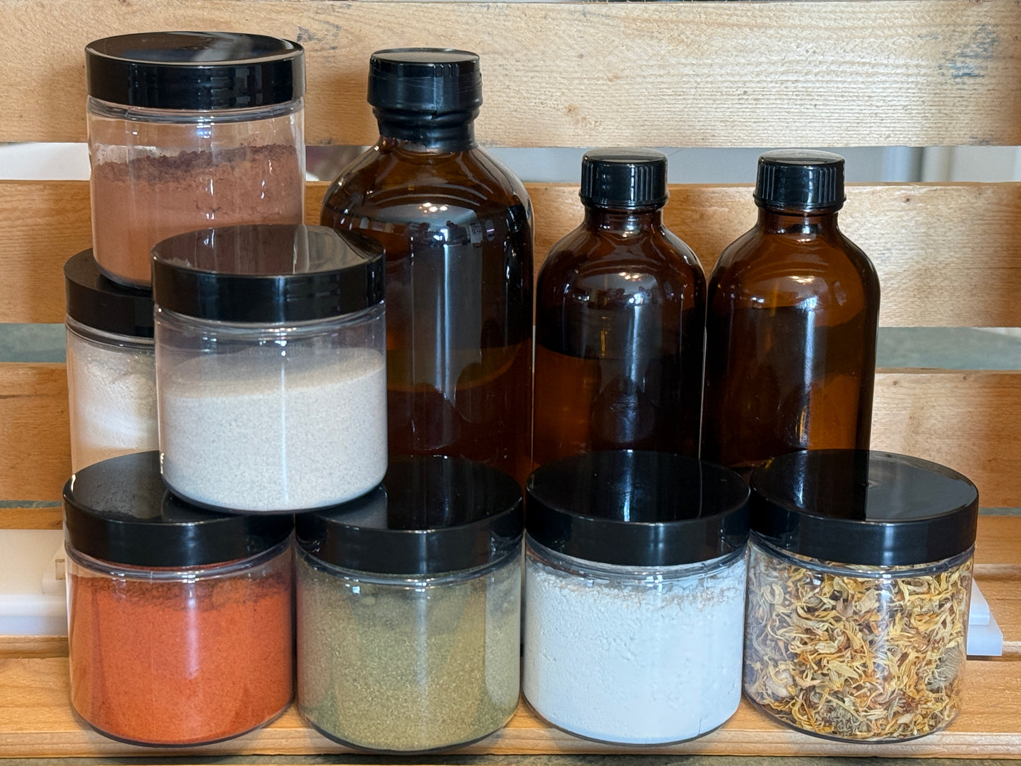 Collection of glass jars with black lids containing various ingredients on a wooden surface.