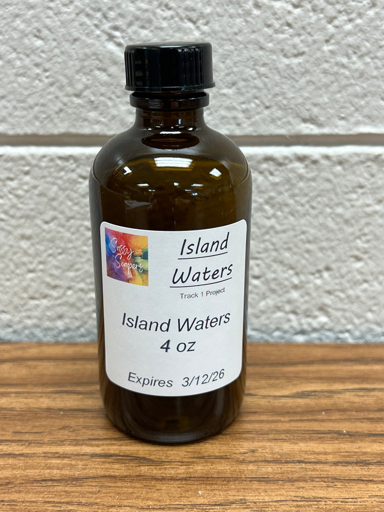4oz Bottle of Island Waters fragrance oil on a wooden surface with a white wall background. Expires 3/12/2026