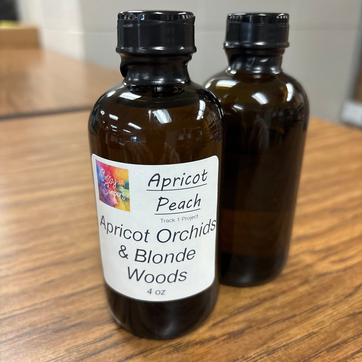 Two brown bottles with Apricot Peach fragrence labels on a wooden surface