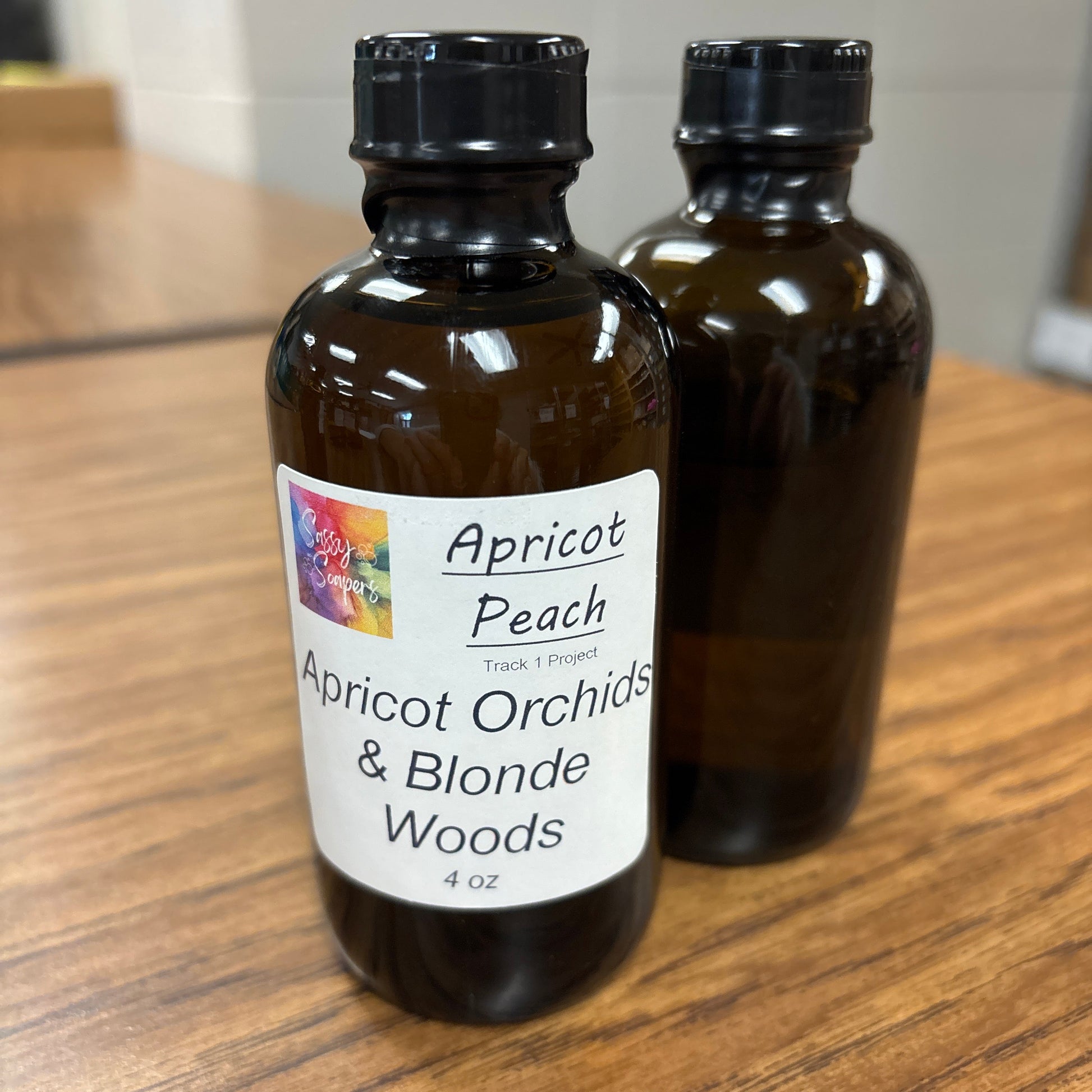 Two brown bottles with Apricot Peach fragrence labels on a wooden surface