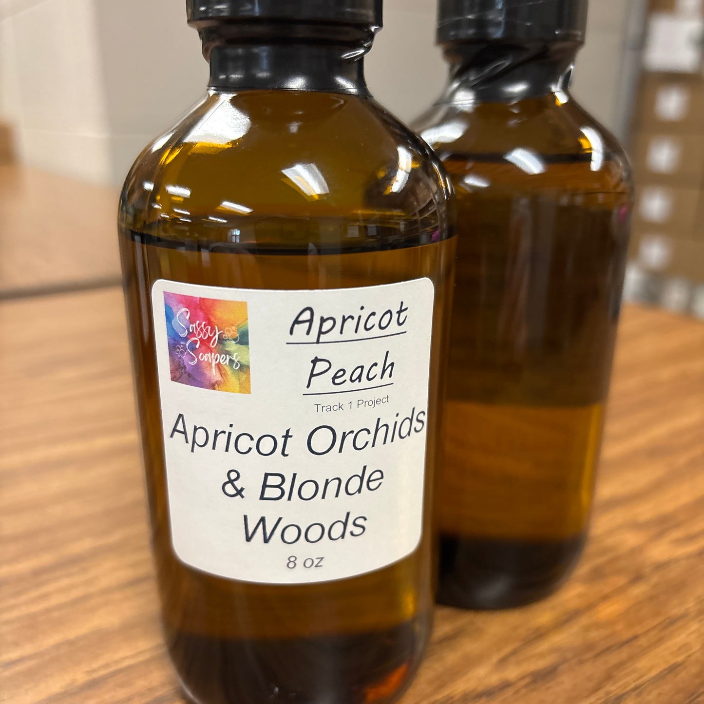 Two brown bottles with Apricot Orchids & Blonde fragrence oils labels on a wooden surface