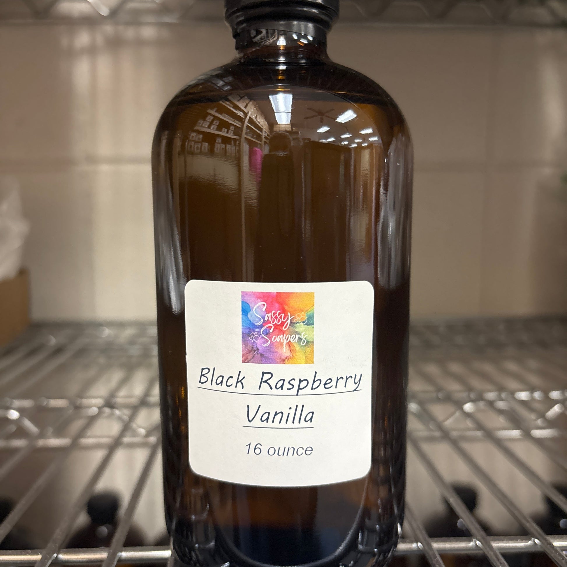 Bottle of Black Raspberry Vanilla fragrence oils with a label on a metal shelf.