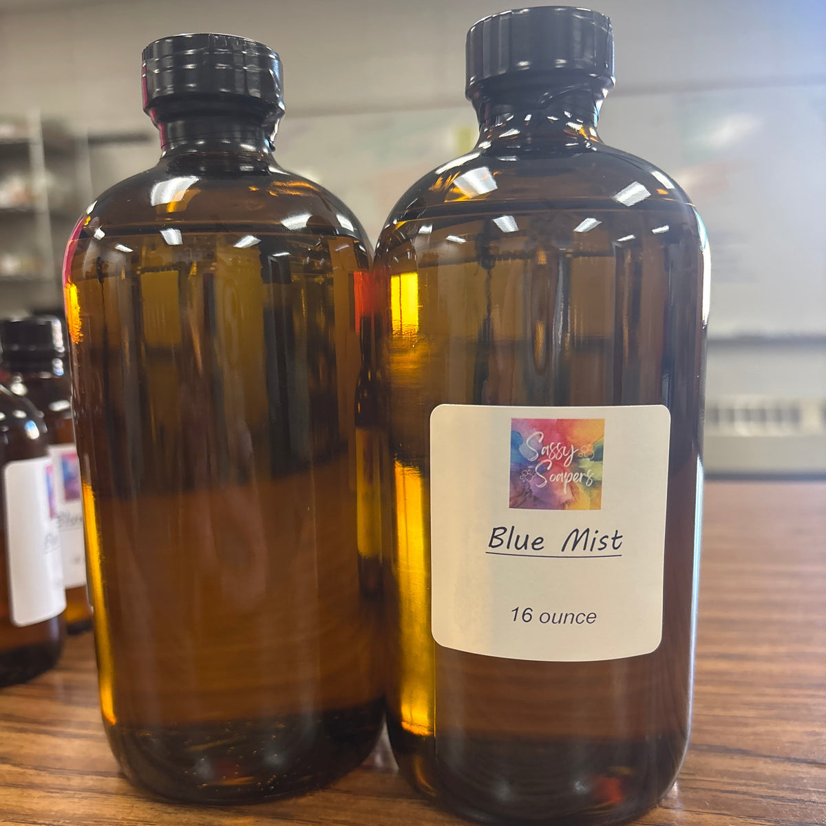 Two bottles of 'Blue Mist' fragrence oil on a wooden surface with a blurred background.