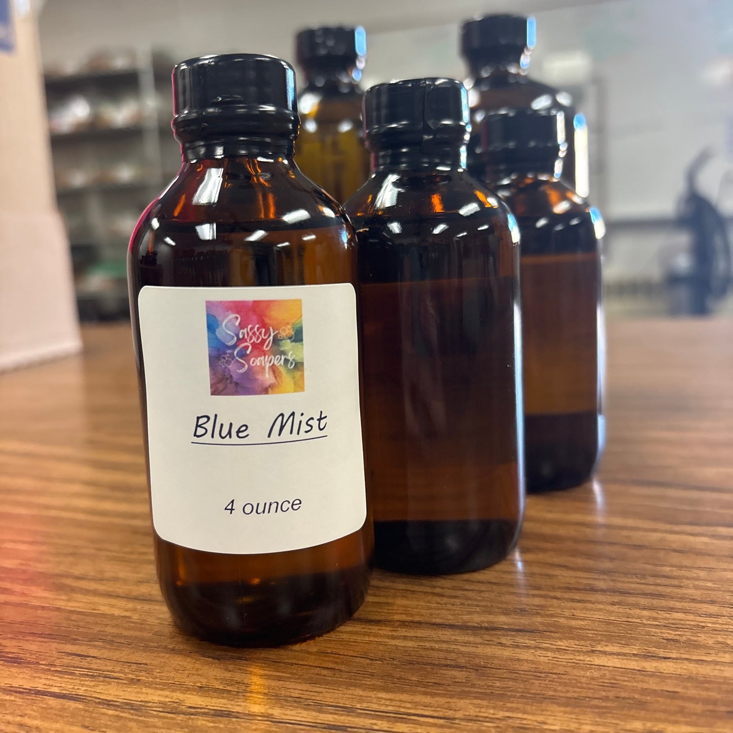 Three amber glass bottles with 'Blue Mist' fragrence oil label on a wooden surface