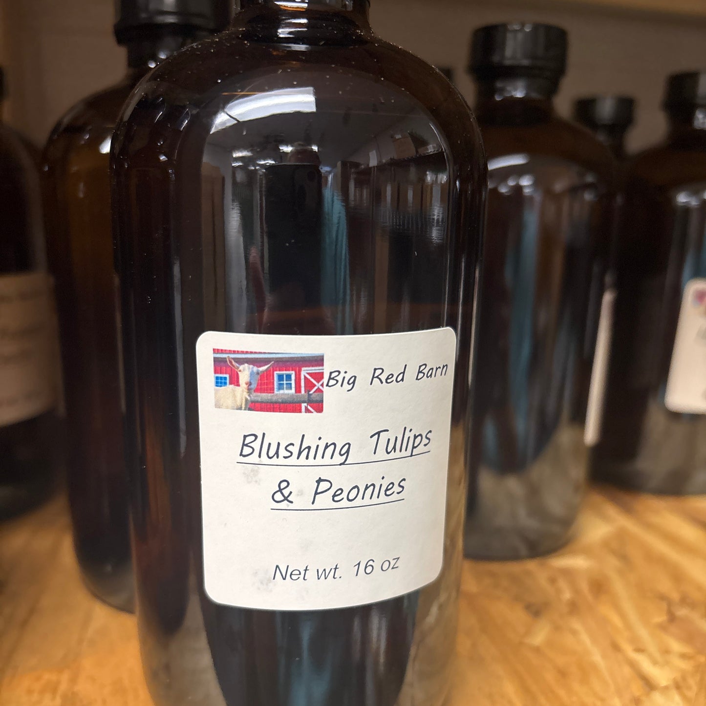 Brown bottle of Blushing Tulips and Peonies with white label on a wooden surface