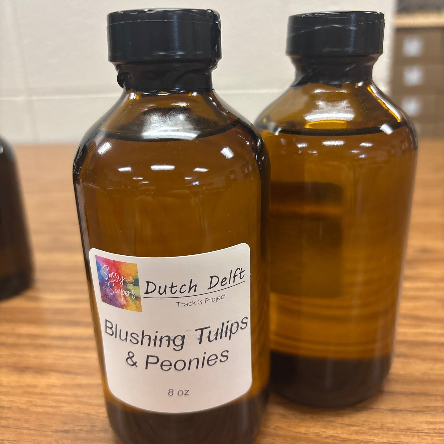 Two bottles of 'Blushing Tulips & Peonies' fragrence by Dutch Delft on a wooden surface.