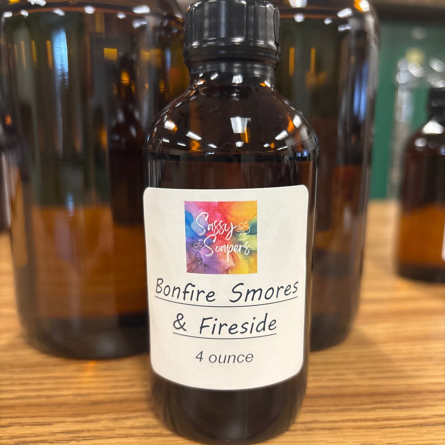 Two bottles of 'Bonfire Smores & Fireside' fragrence oils on a wooden surface with a colorful label.