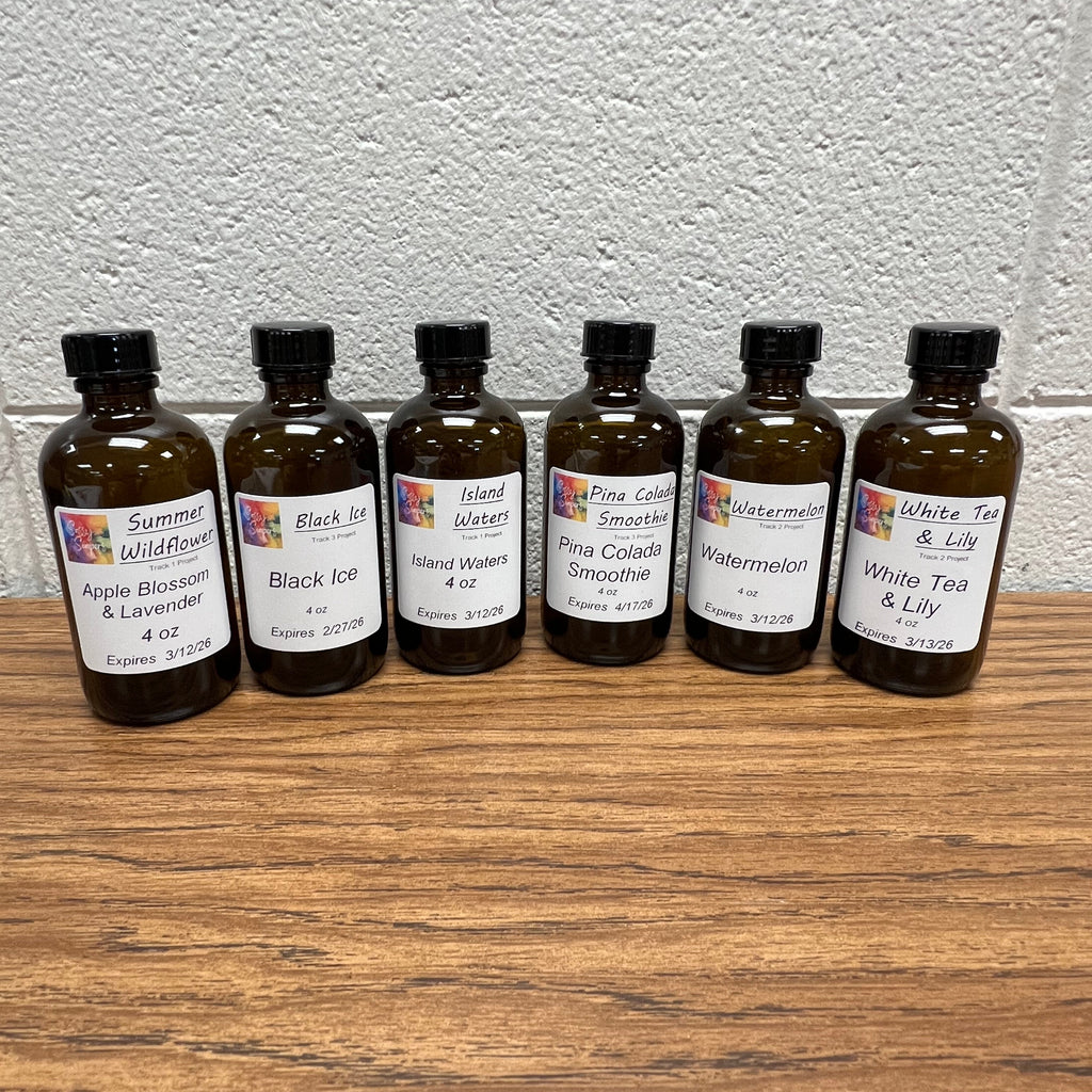 Six small brown bottles of fragrance oils with labels on a white wall and wooden surface.