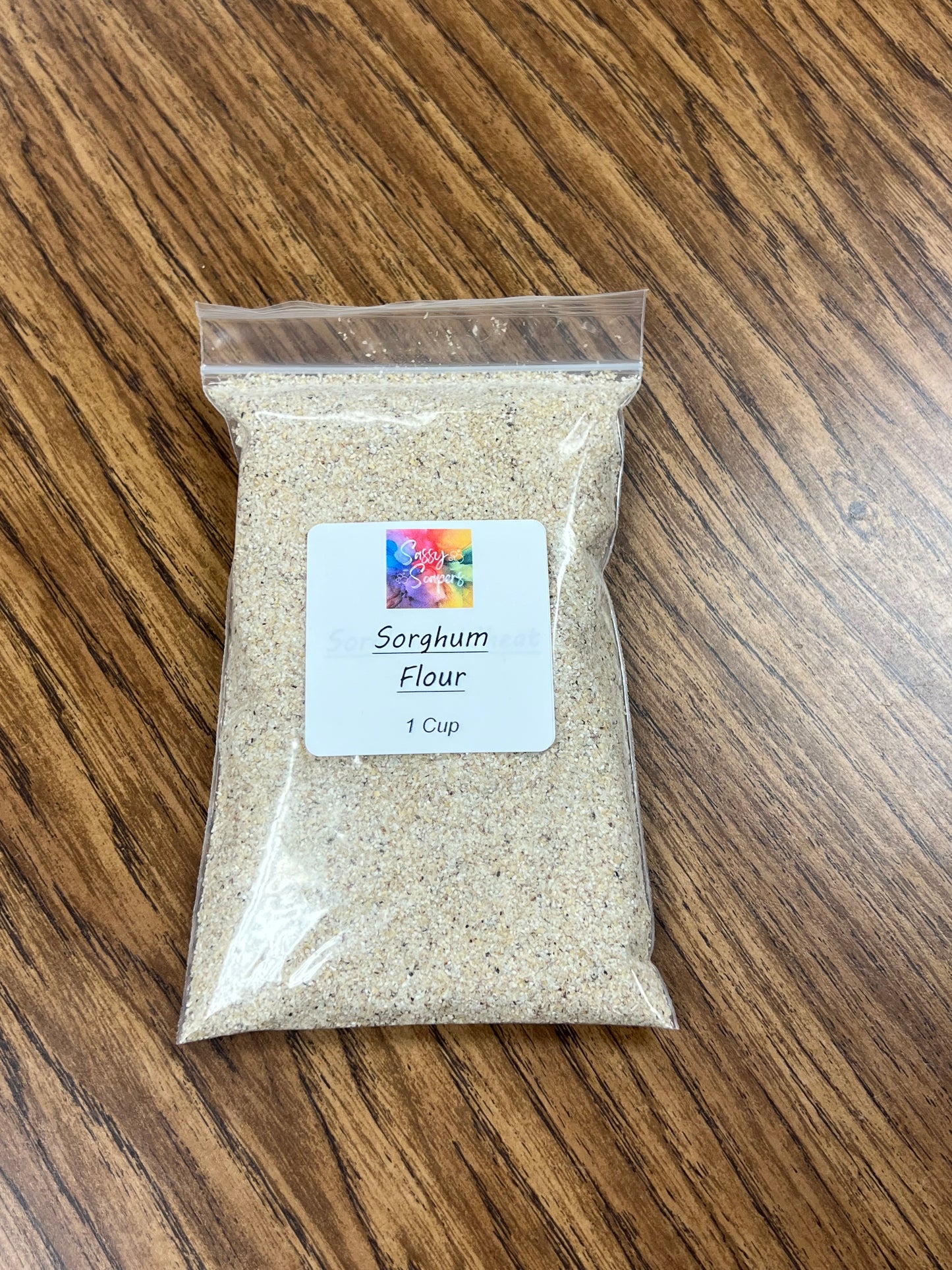 Clear plastic bag containing 1 cup of sorghum flour on woodgrain surface.