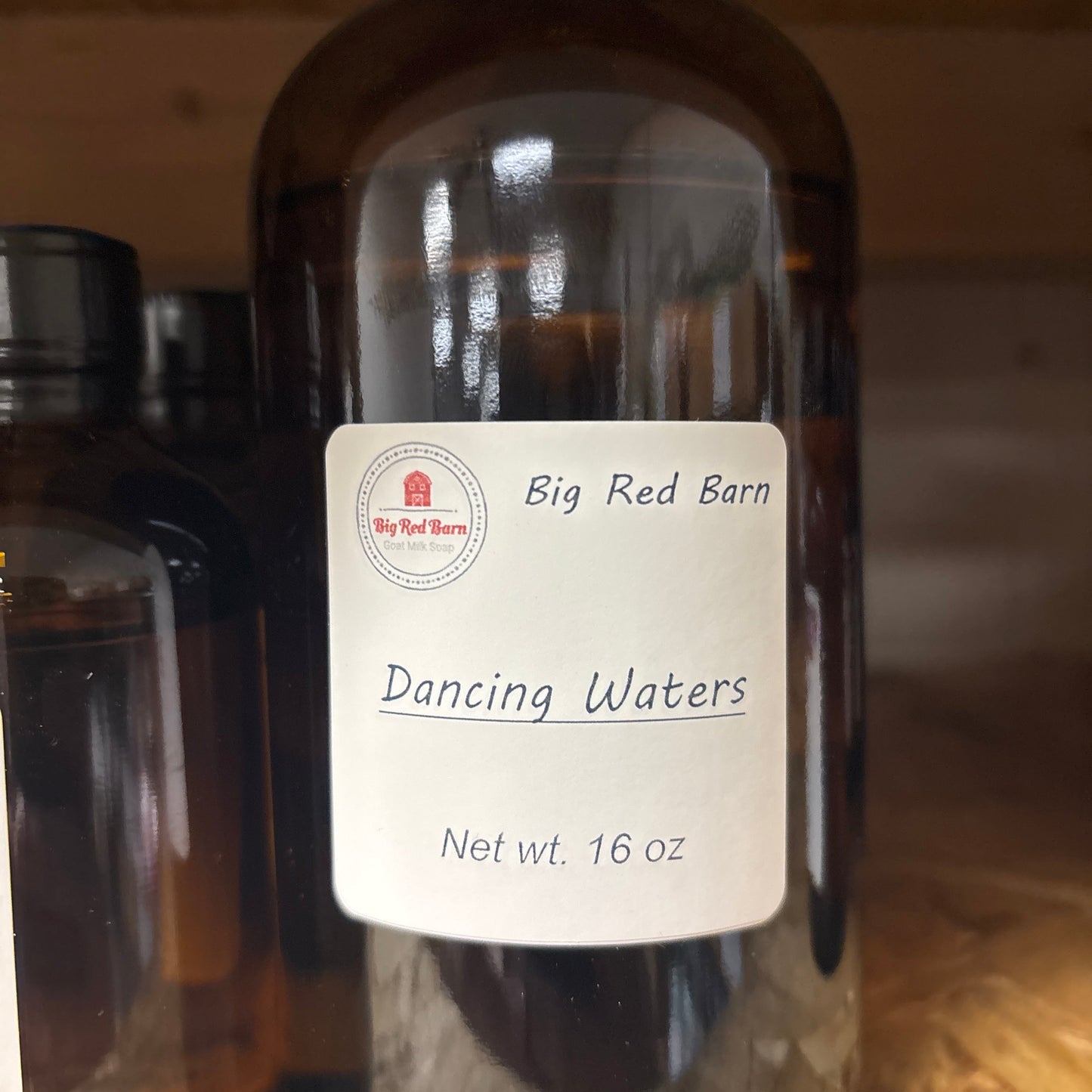 Bottle of 'Big Red Barn Dancing Waters' fragrence oils with a label on a wooden surface.