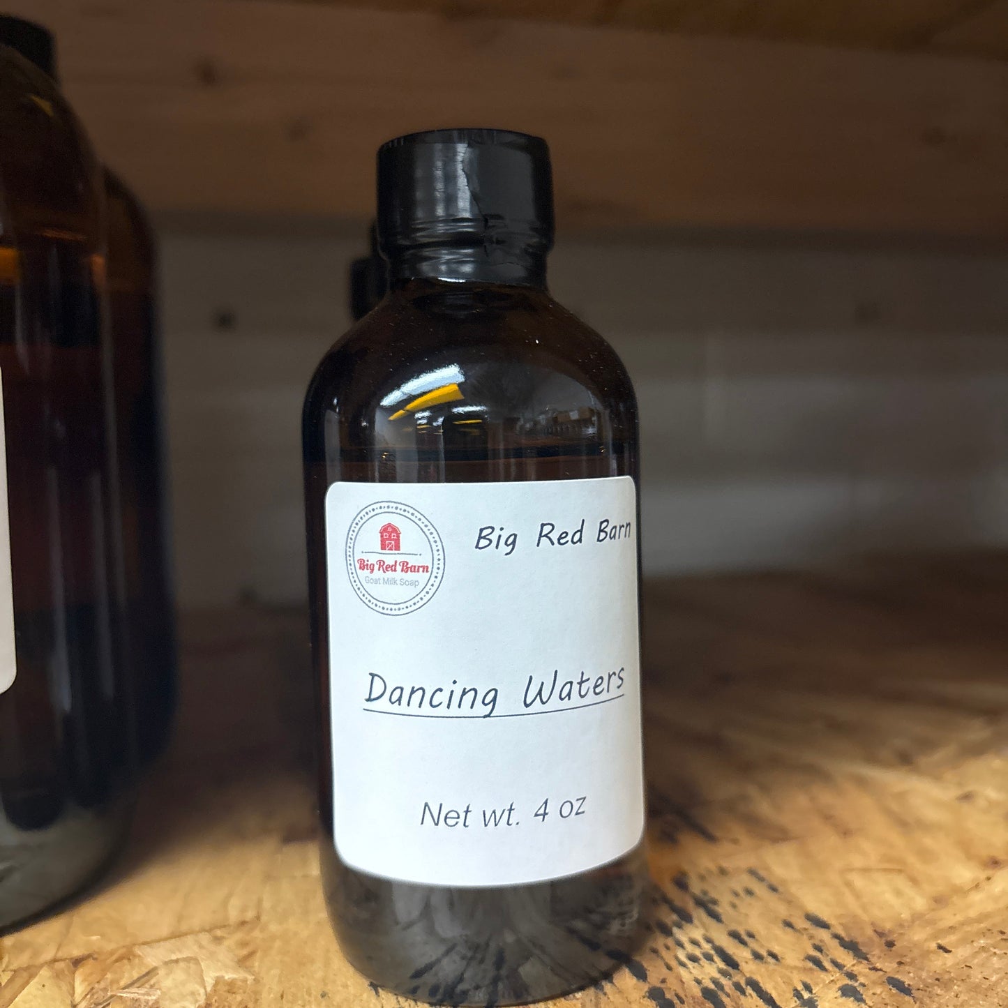 Bottle of 'Big Red Barn' Dancing waters fragrence oil product with a label on a wooden surface