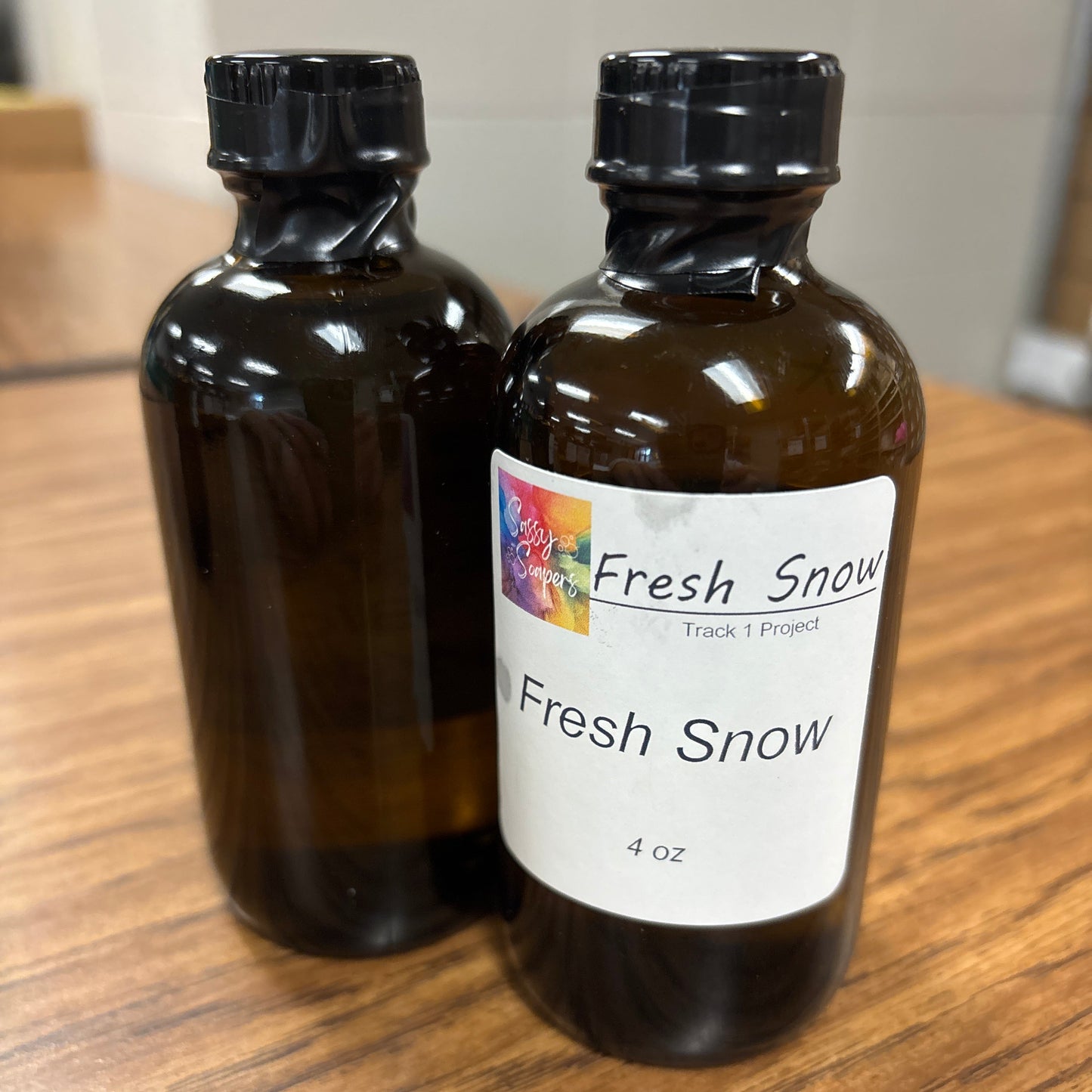 Amber glass bottle labeled 'Fresh Snow' fragrence oils on a wooden surface