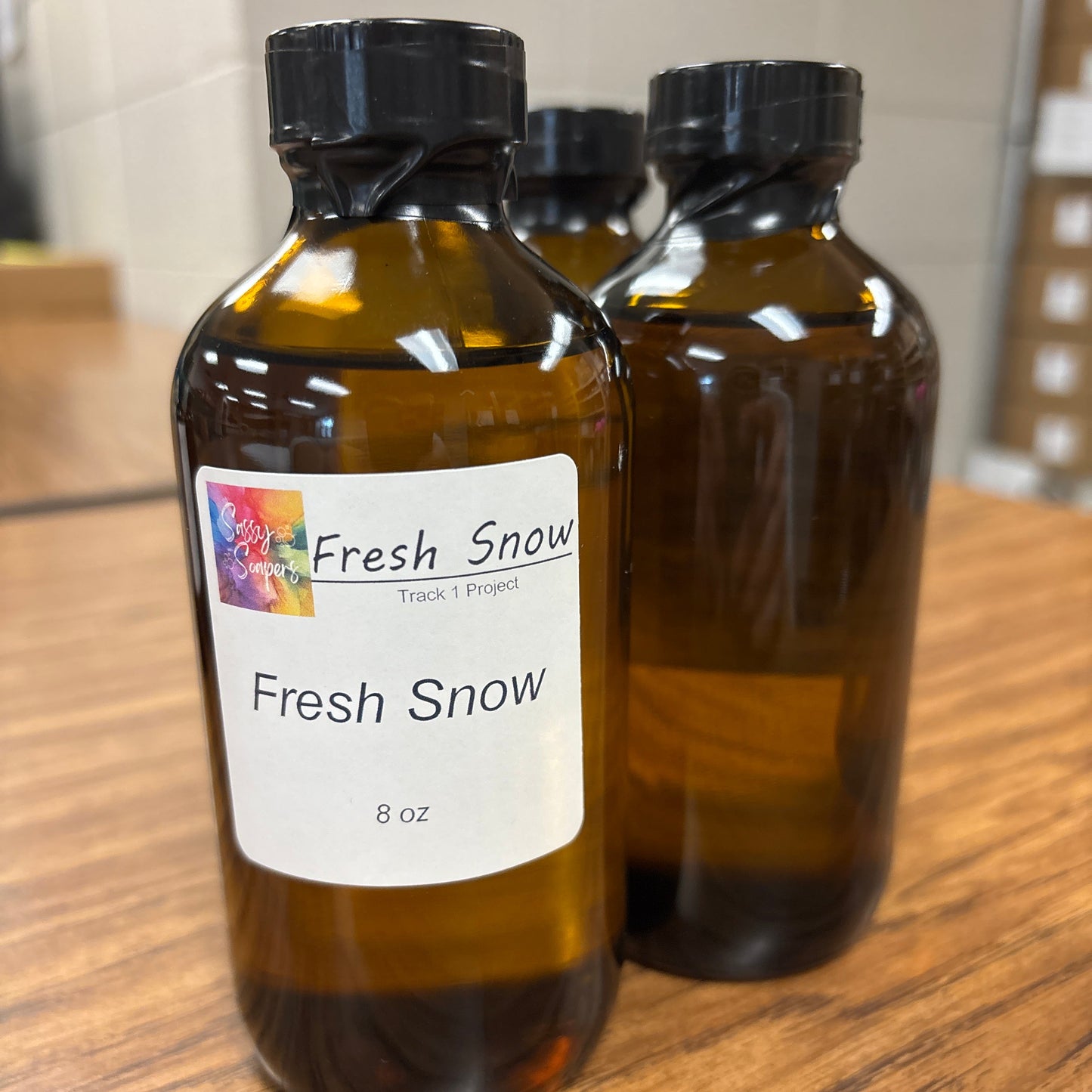 Two brown bottles labeled 'Fresh Snow' fragrence on a wooden surface.