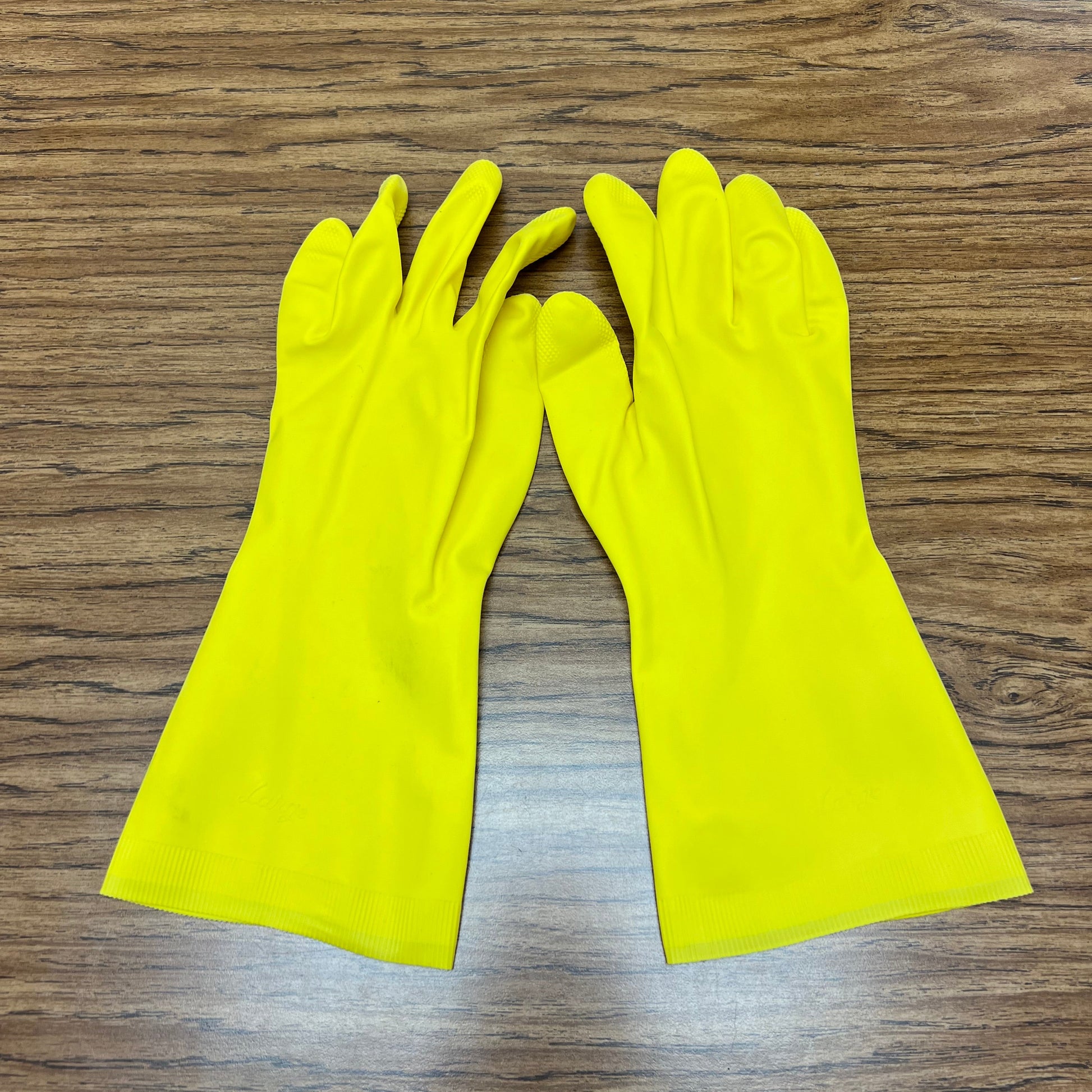 Pair of yellow, medium size chemical resistant gloves for soap making on woodgrain background.