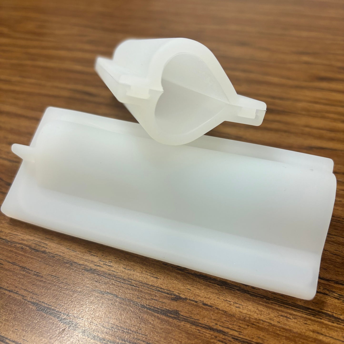 Two white plastic molds designed for crafting embeds, placed on a wooden surface.