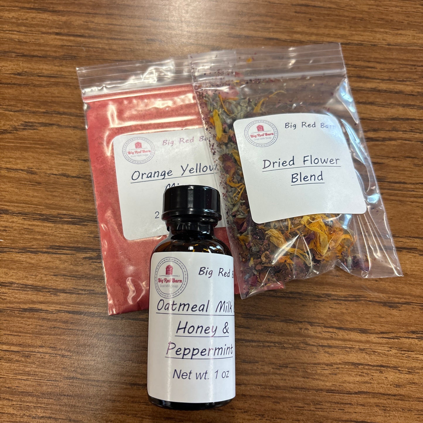 Packaged dried flower blend and small oatmeal milk honey & peppermint fragrence oil bottle on a wooden surface