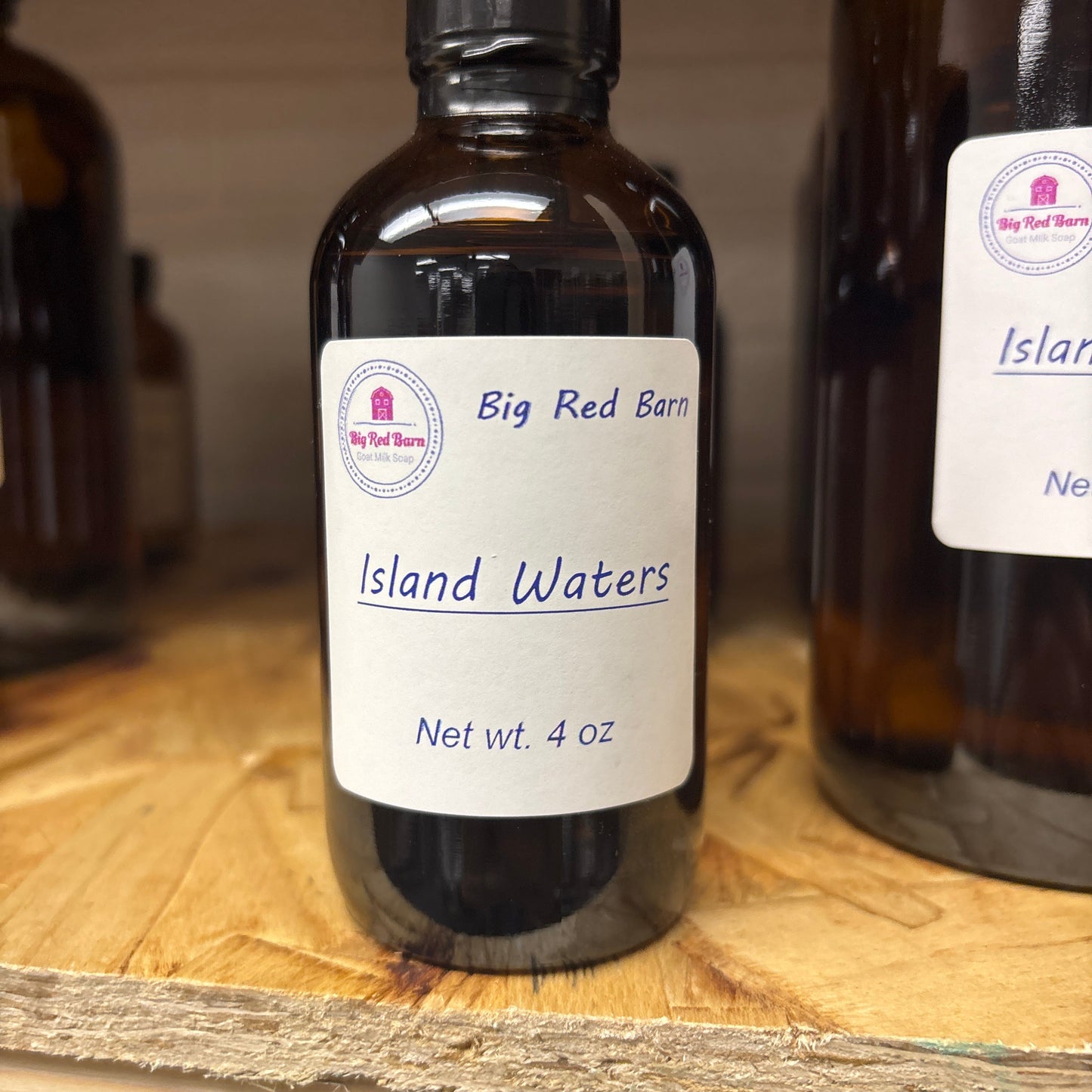 Two bottles of 'Big Red Barn Island Waters' fragrance on a wooden surface