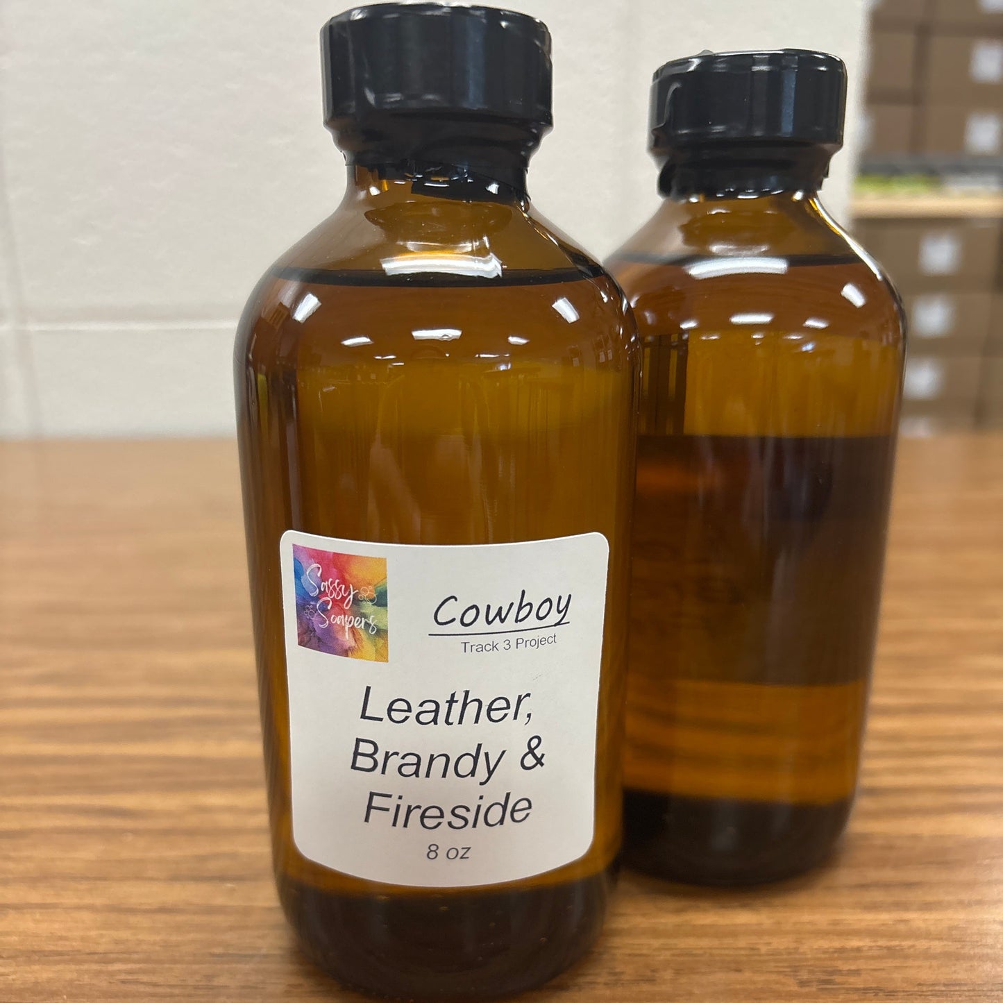 Two bottles of 'Cowboy Leather Brandy Fireside' fragrence on a wooden surface.