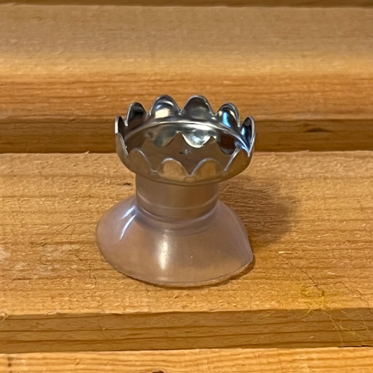 A silver-colored metal soap holder with a scalloped edge design, placed on a wooden surface.
