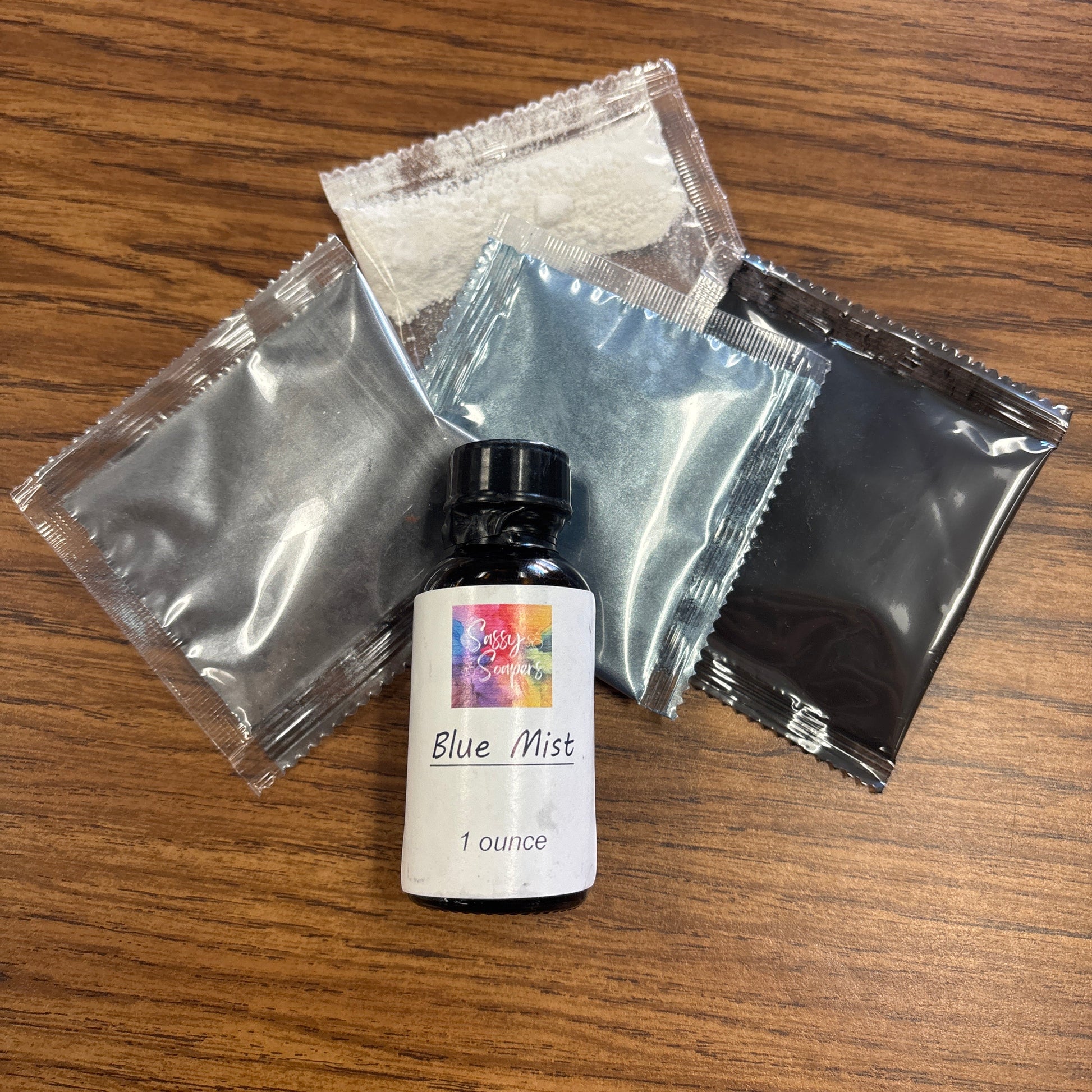 Small bottle with Blue mist fragrence oil label on a wooden surface, surrounded by small packets on a wodden surface 