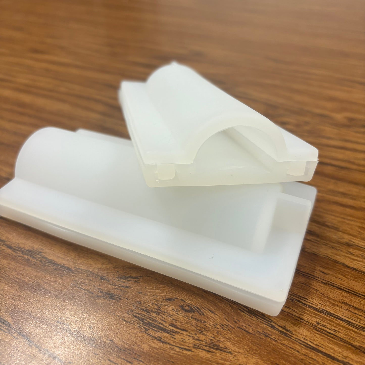 Two white plastic molds designed for crafting embeds, placed on a wooden surface.