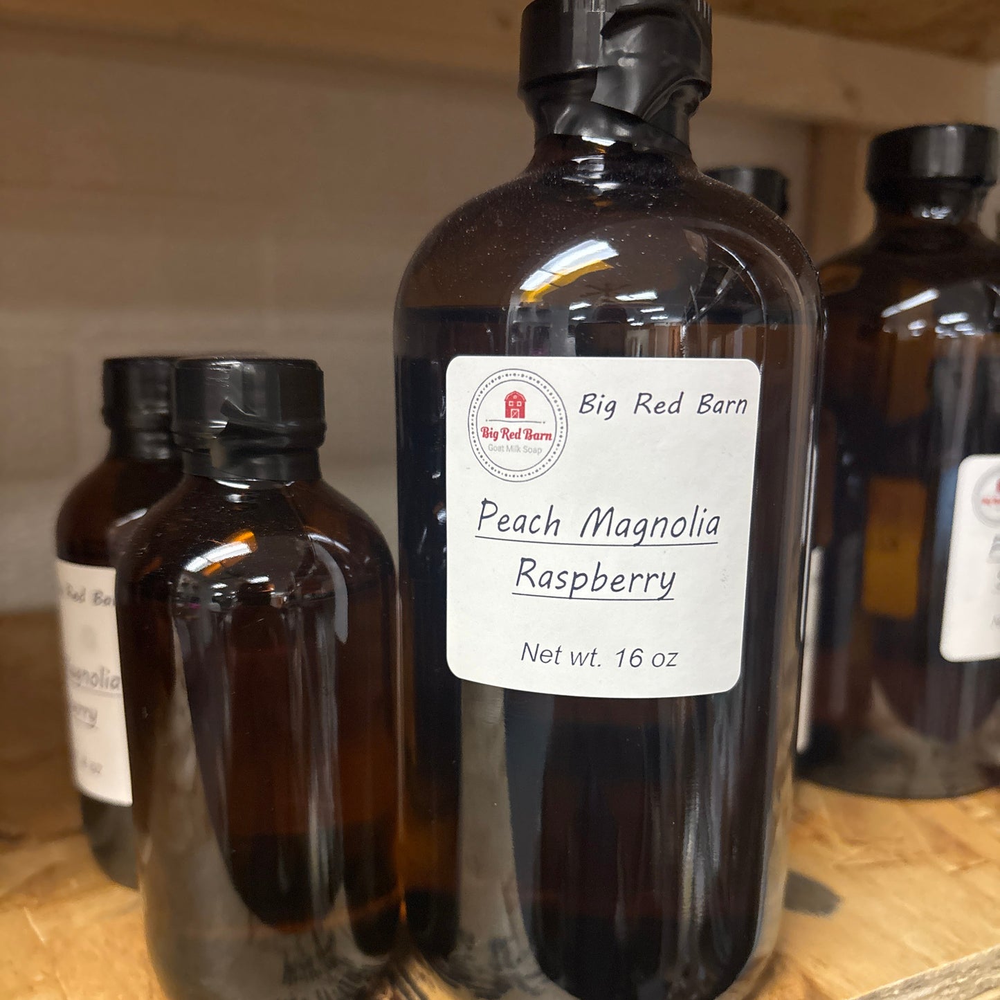 Two brown glass bottles with Peach Magnolia Raspberry fragrence oils labels on a wooden surface
