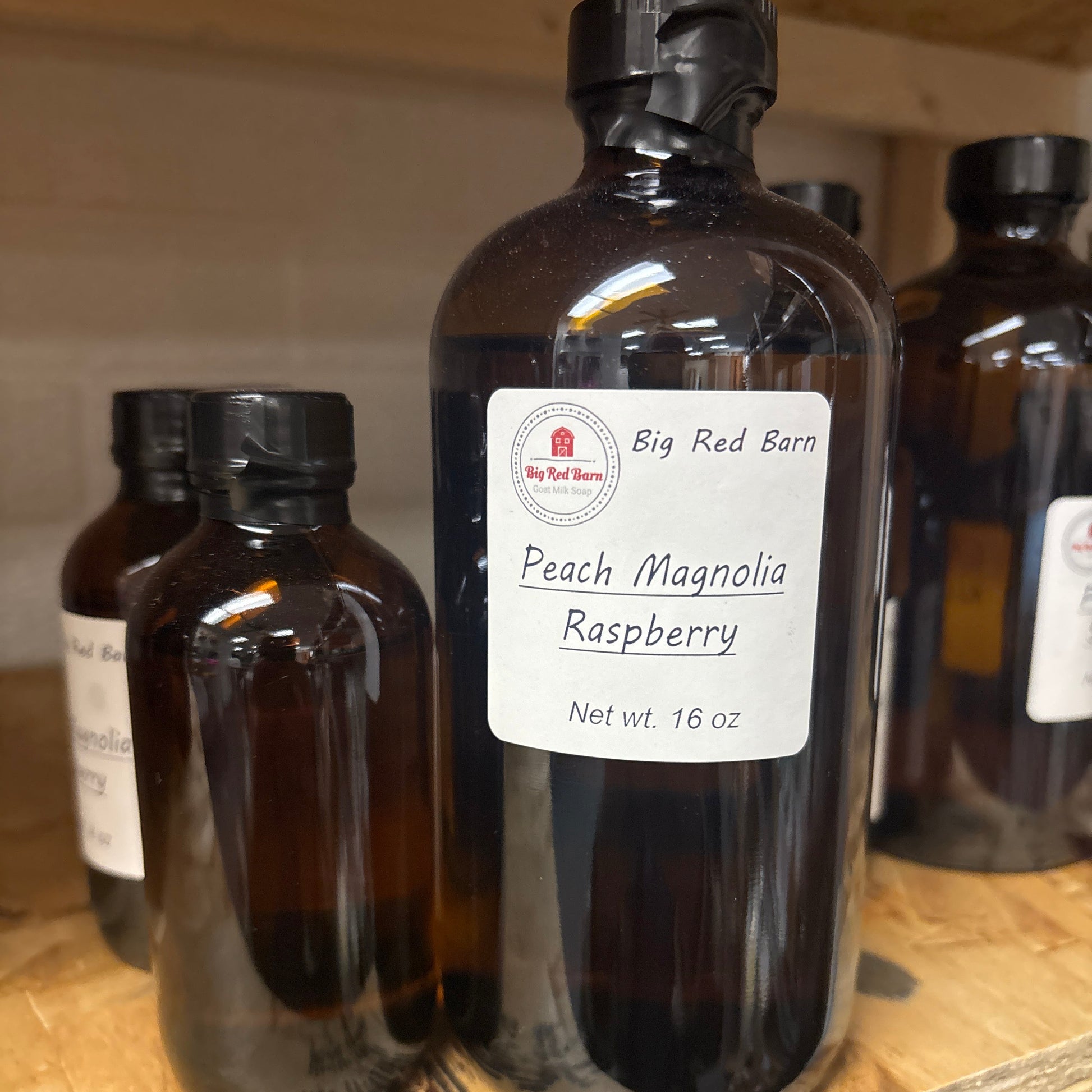 Two brown glass bottles with Peach Magnolia Raspberry fragrence oils labels on a wooden surface