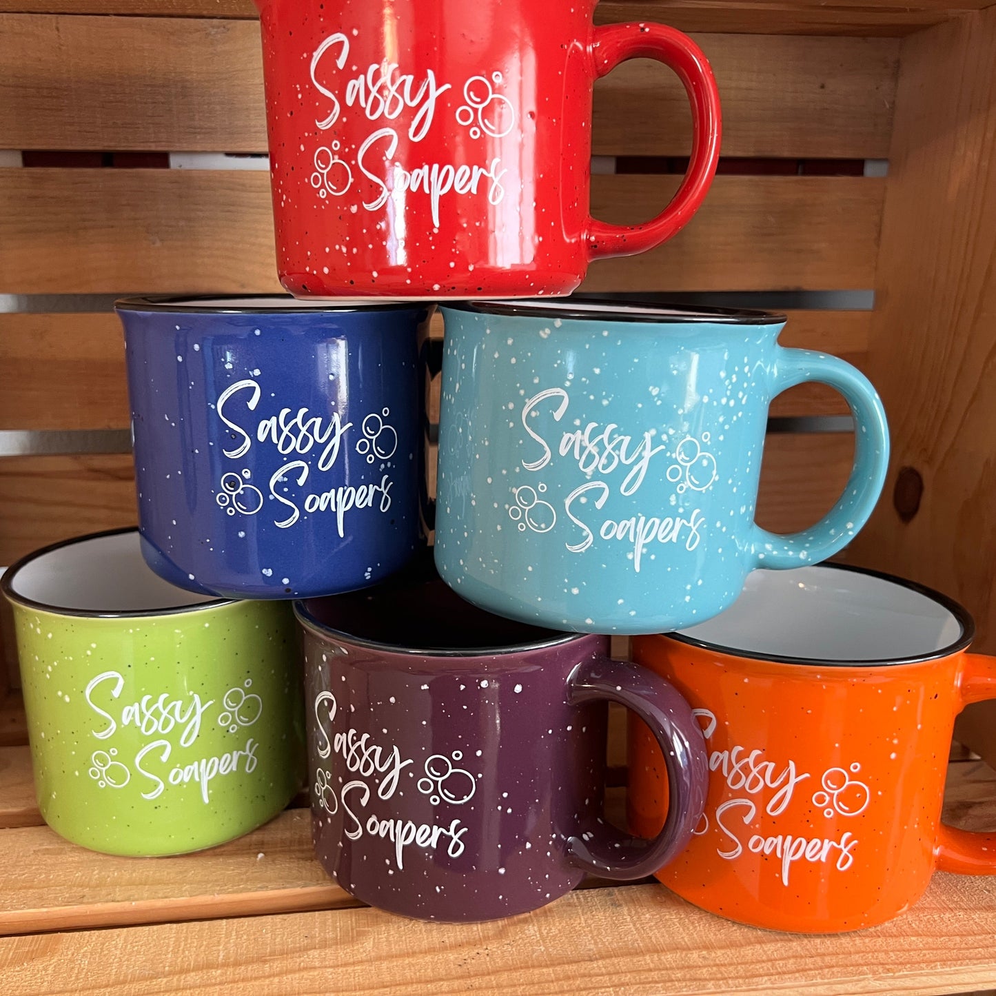 A set of ceramic mugs with 'Sassy Soapers' text and soap bubble designs, displayed in a variety of colors.