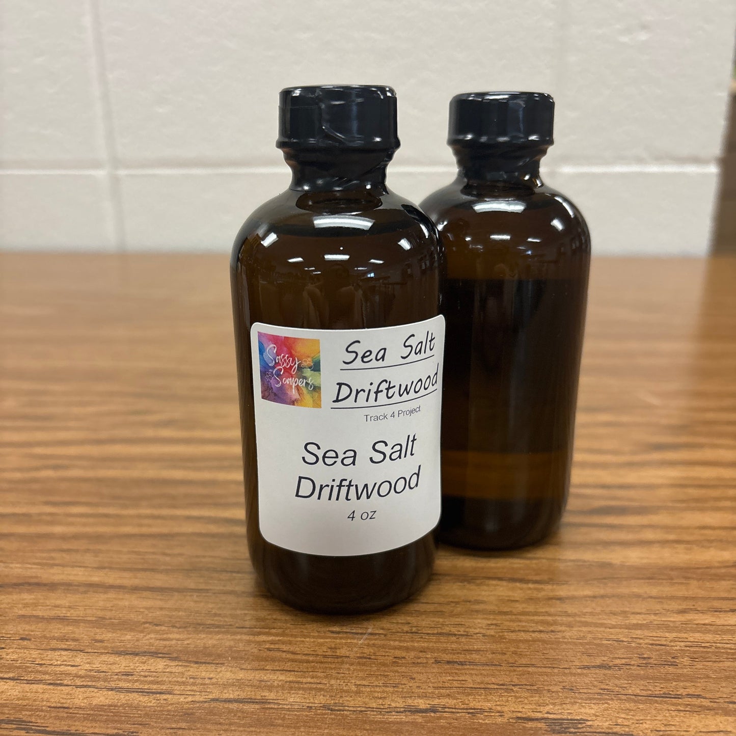 Two bottles of Sea Salt Driftwood fragrence oils on a wooden surface with a white tile background