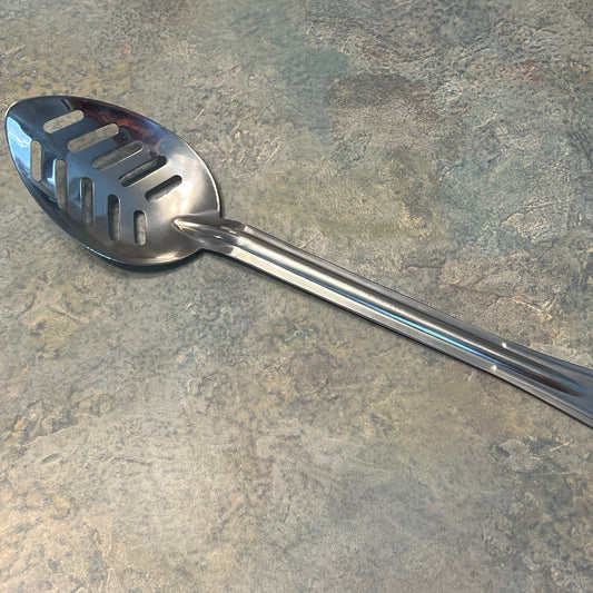 A stainless steel slotted spoon with a long handle, laying on a speckled stone surface.