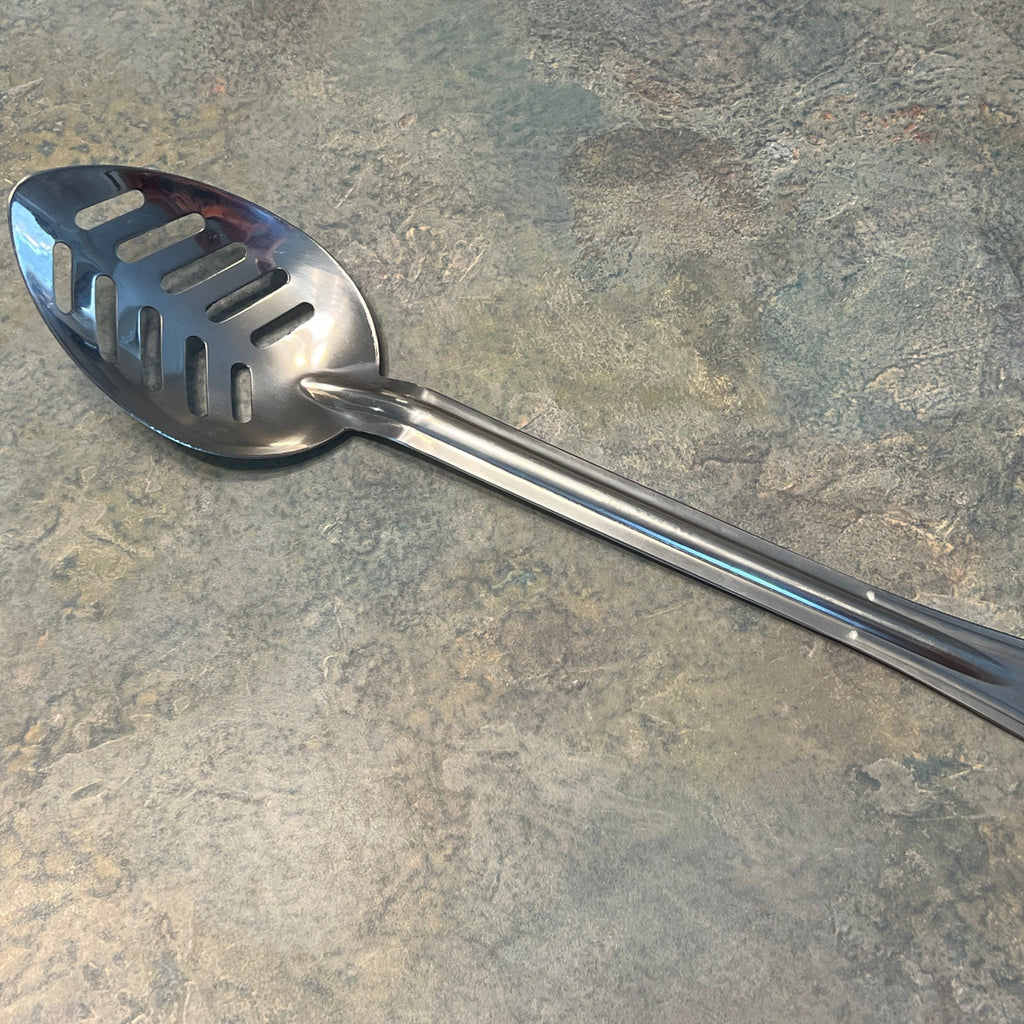 A stainless steel slotted spoon with a long handle, laying on a speckled stone surface.