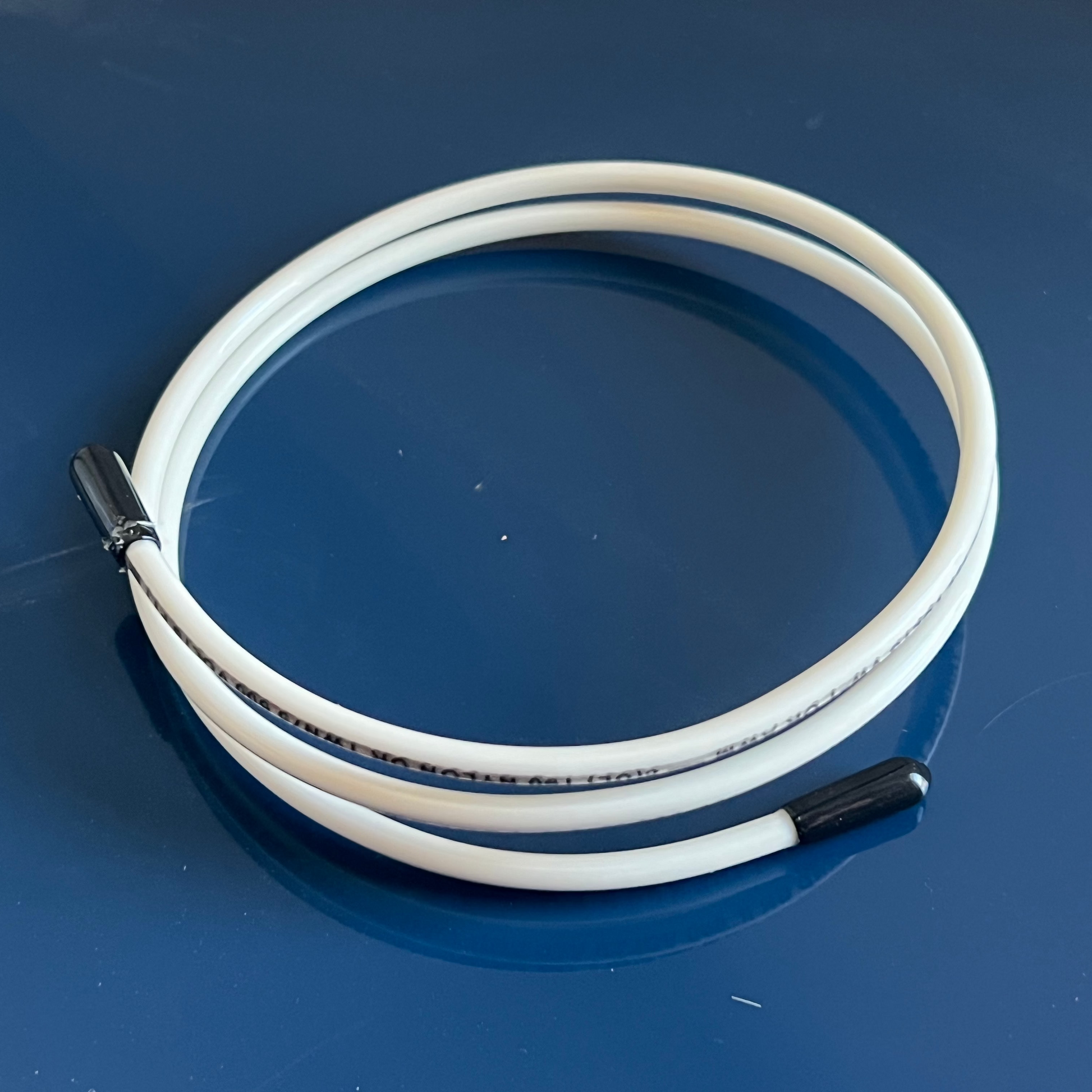 A white swirl tool with black accents designed for creating patterns in soap batches, displayed on a blue background.