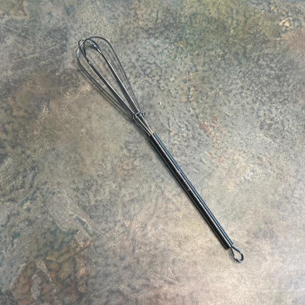 A small stainless steel whisk lying on a textured surface.