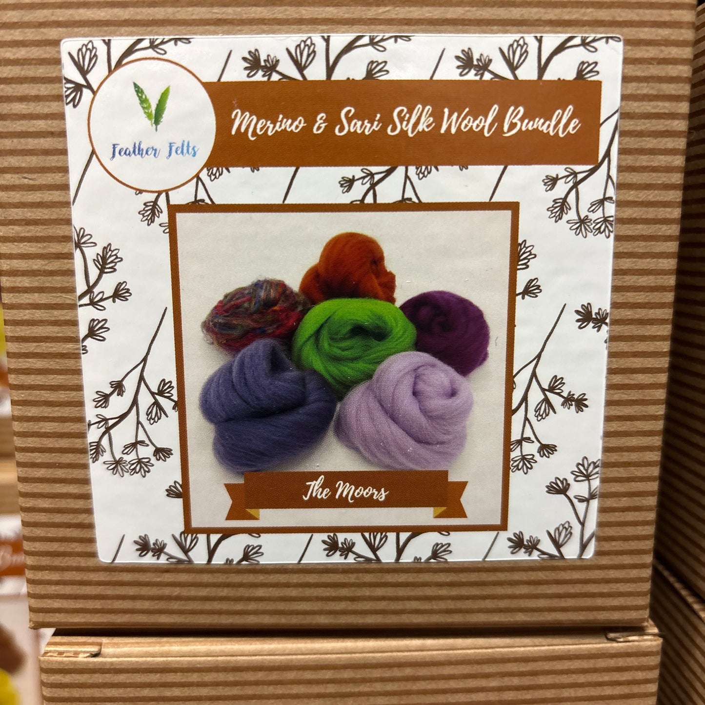 Cardboard box with a decorative label featuring colorful wool bundles and branding text.