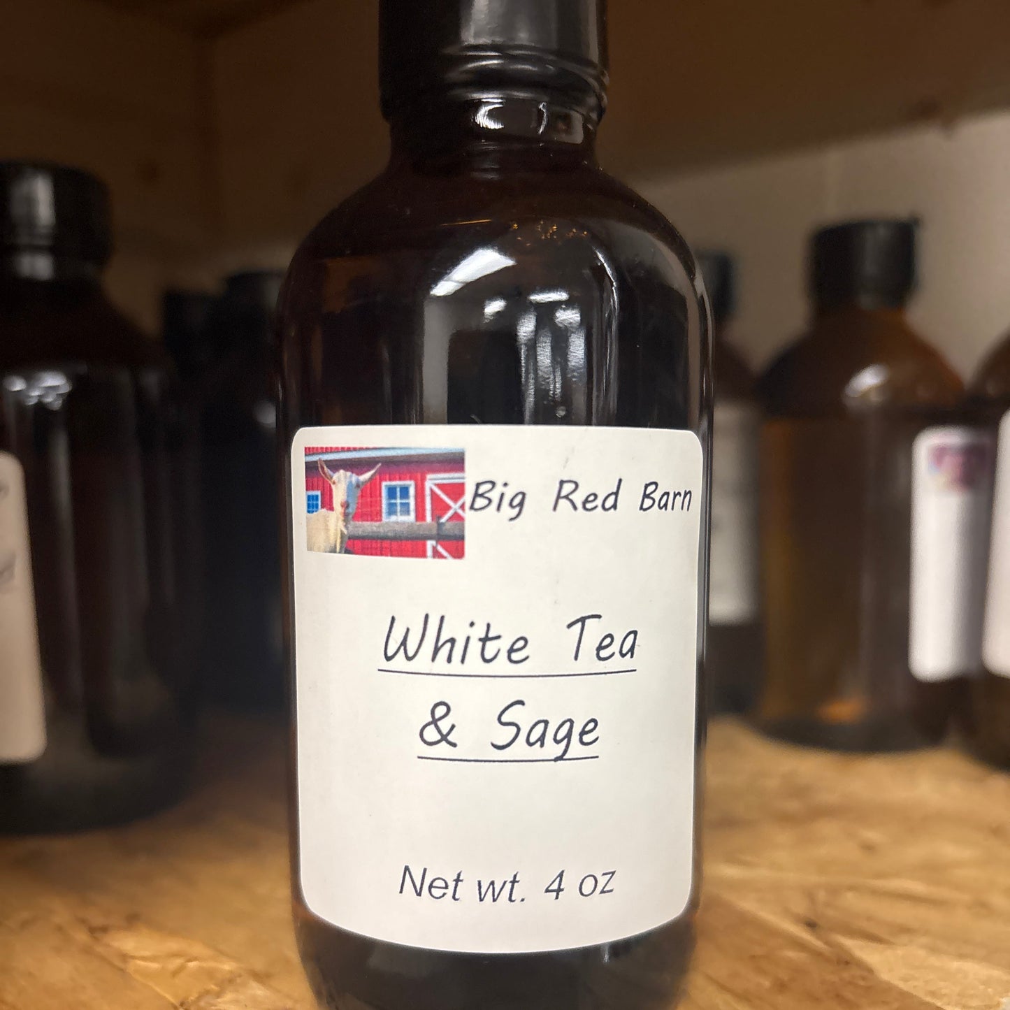 A brown bottle labeled 'White tea and sage'  fragrence oils from Big Red Barn, on a wooden surface