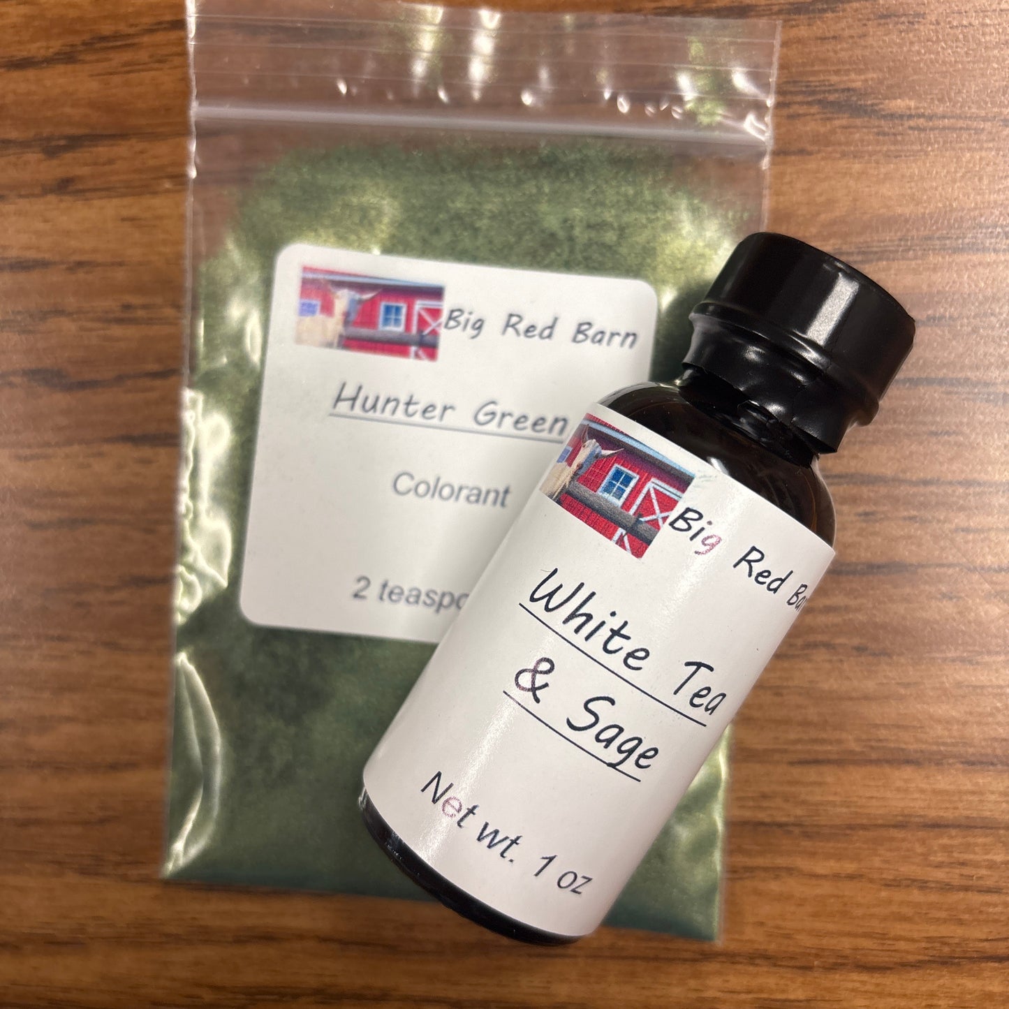 Small bottle labeled 'White Tea & Sage' fragrence oils on a wooden surface with a green colorant bag underneath.
