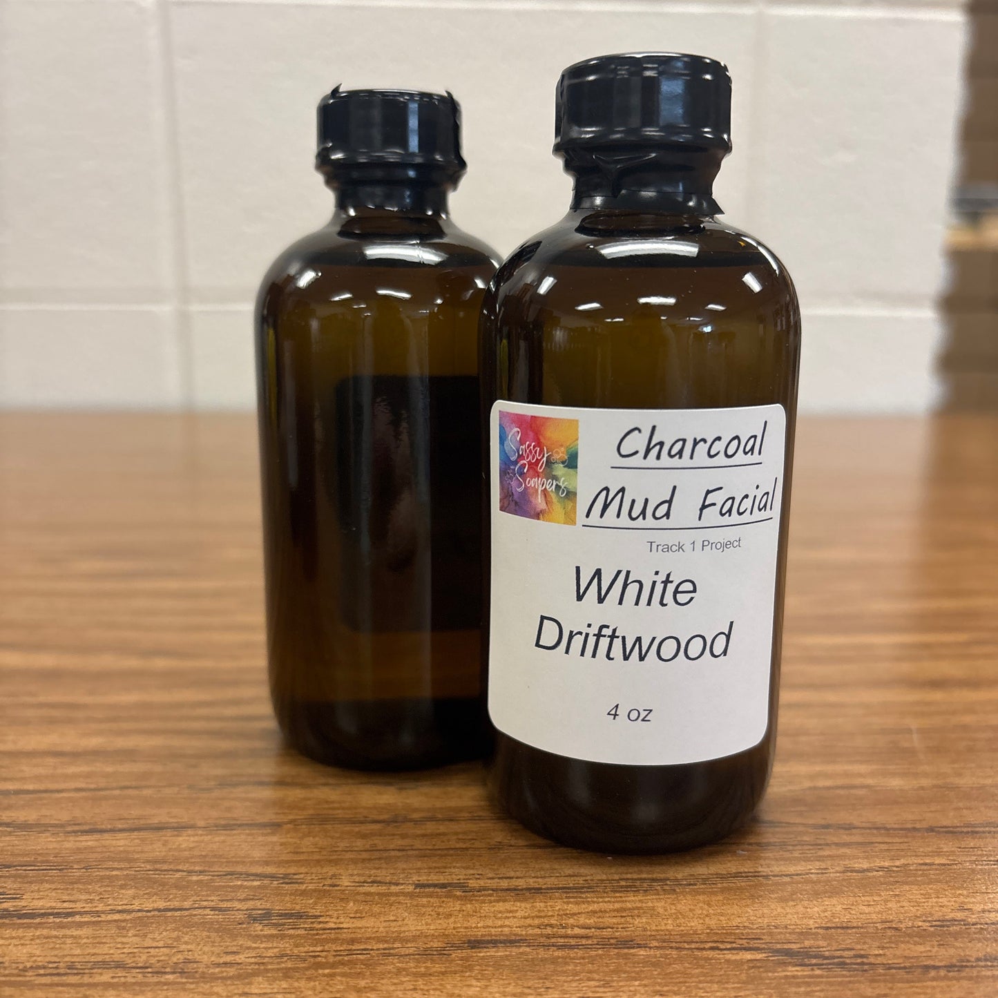Two bottles of 'Charcoal Mud Facial' White driftwood fragrence oils on a wooden surface.