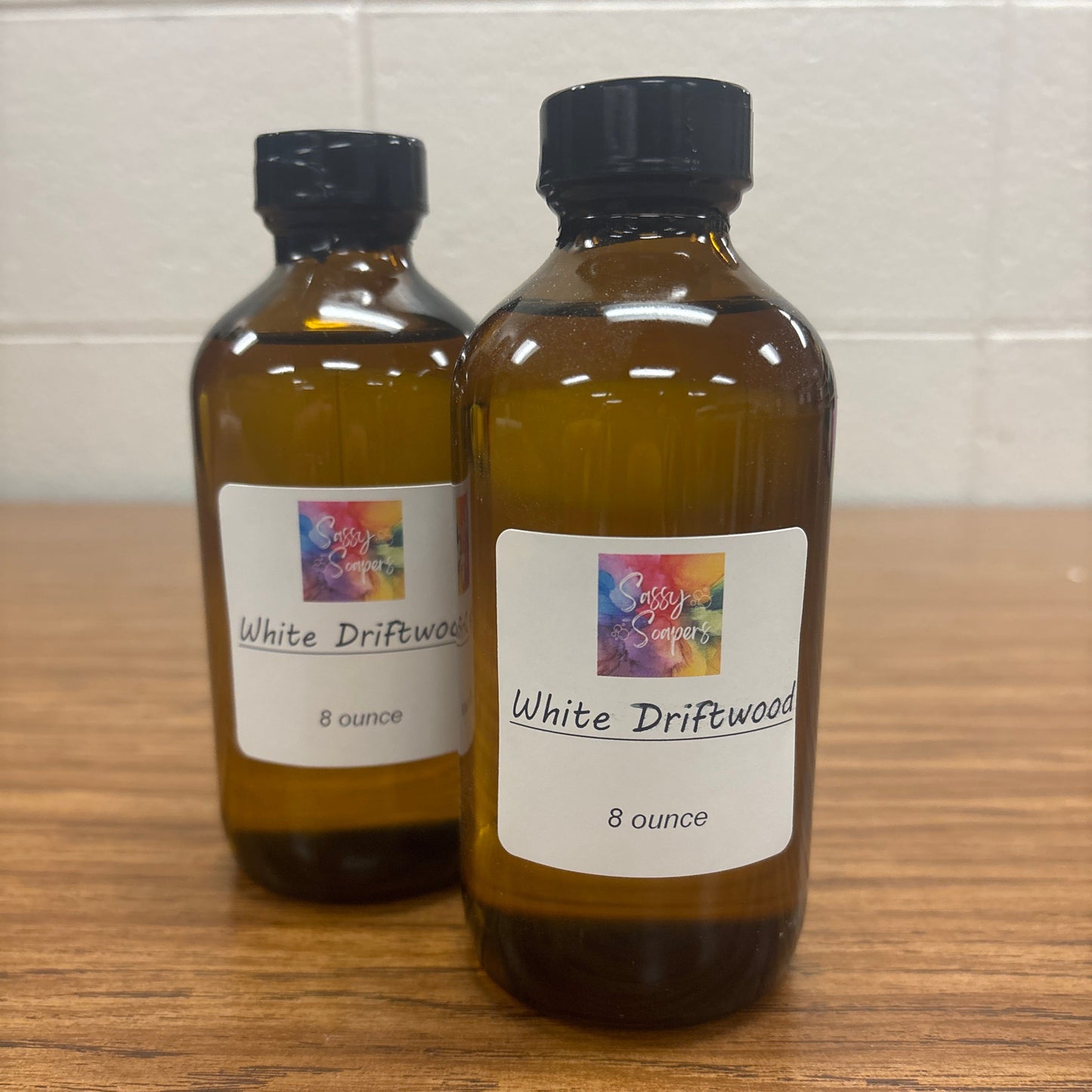 Two bottles of 'White Driftwood' fragrence oils on a wooden surface.