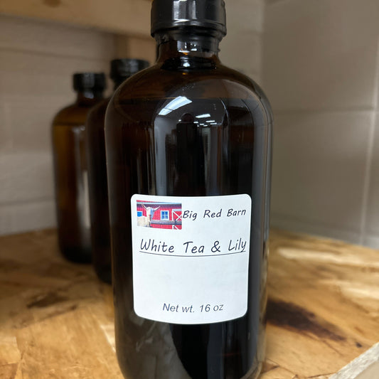 A bottle of fragrance oil labeled 'White tea & Lily' from Big Red Barn, on a wooden surface.