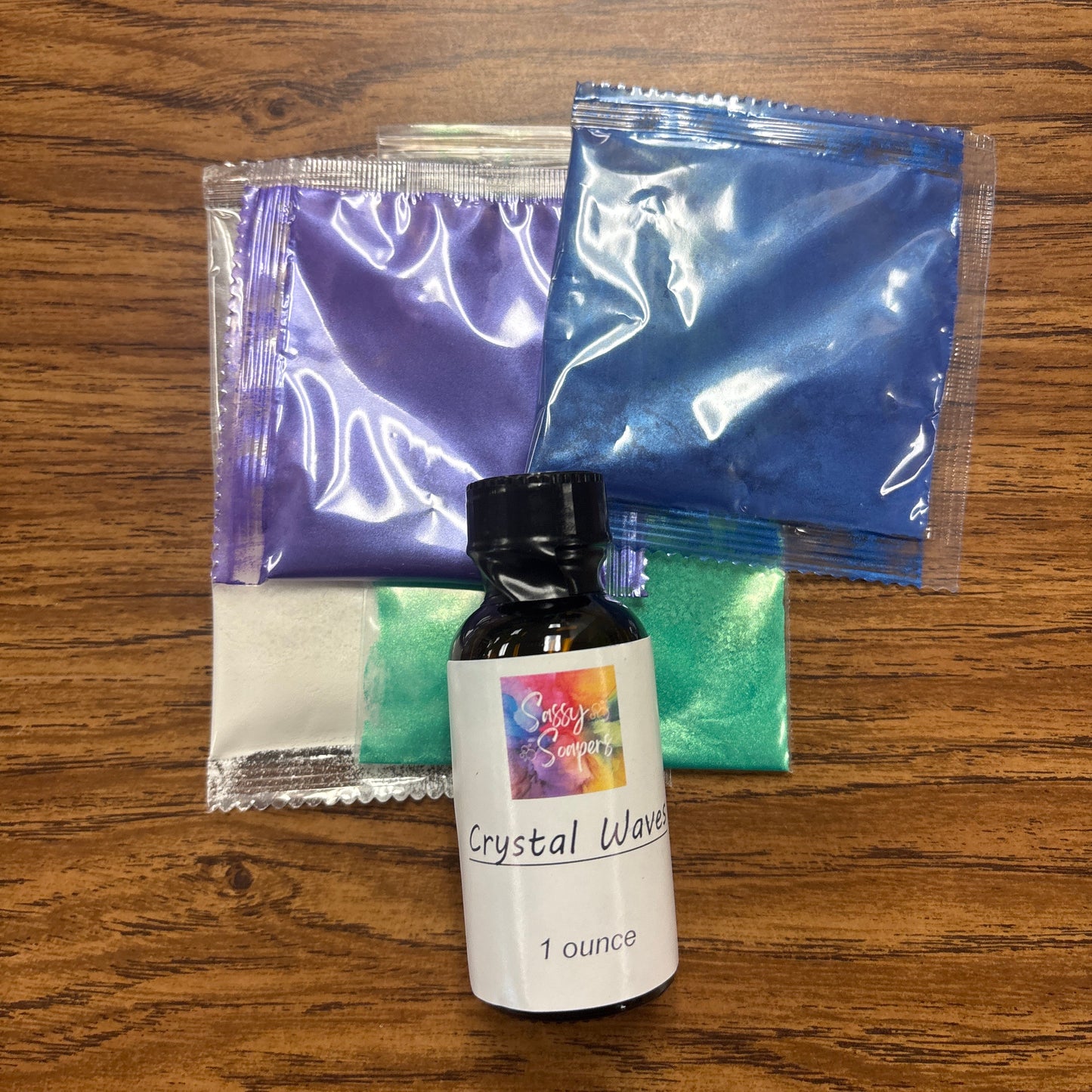 Bottle of 'Crystal Wave' on a wooden surface with two blue packets and a green cloth underneath.