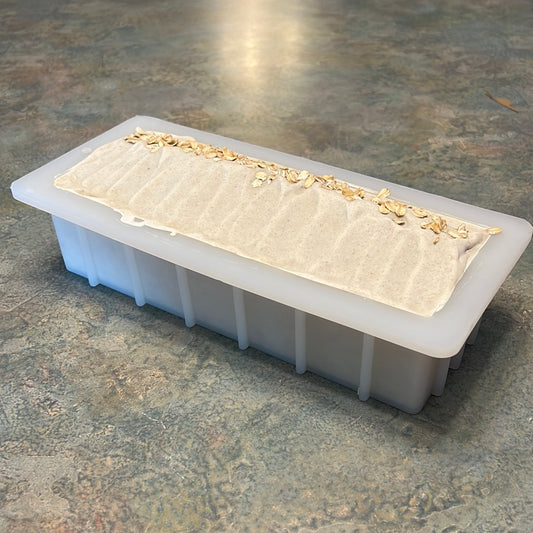 A silicone loaf soap mold filled with soap, adorned with decorative toppings, on a kitchen countertop.